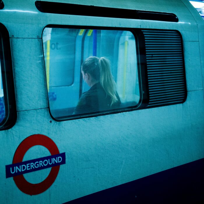 A woman seen through the window of a London Underground train at night.