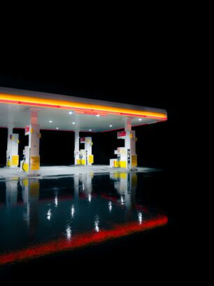 Photo of a gas station at night, the glowing lights reflected in the water. 