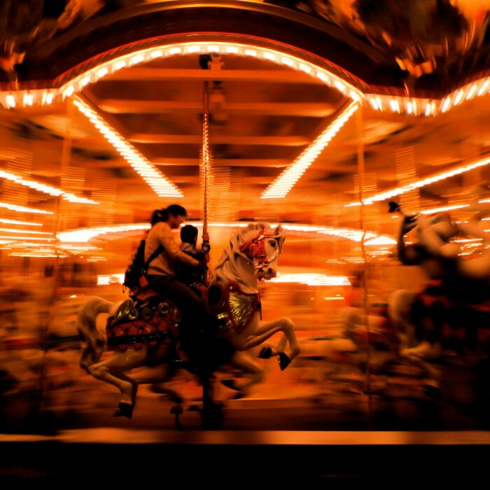 Neon-lit carnival rides blurred in motion, evoking chaos and lost youth.