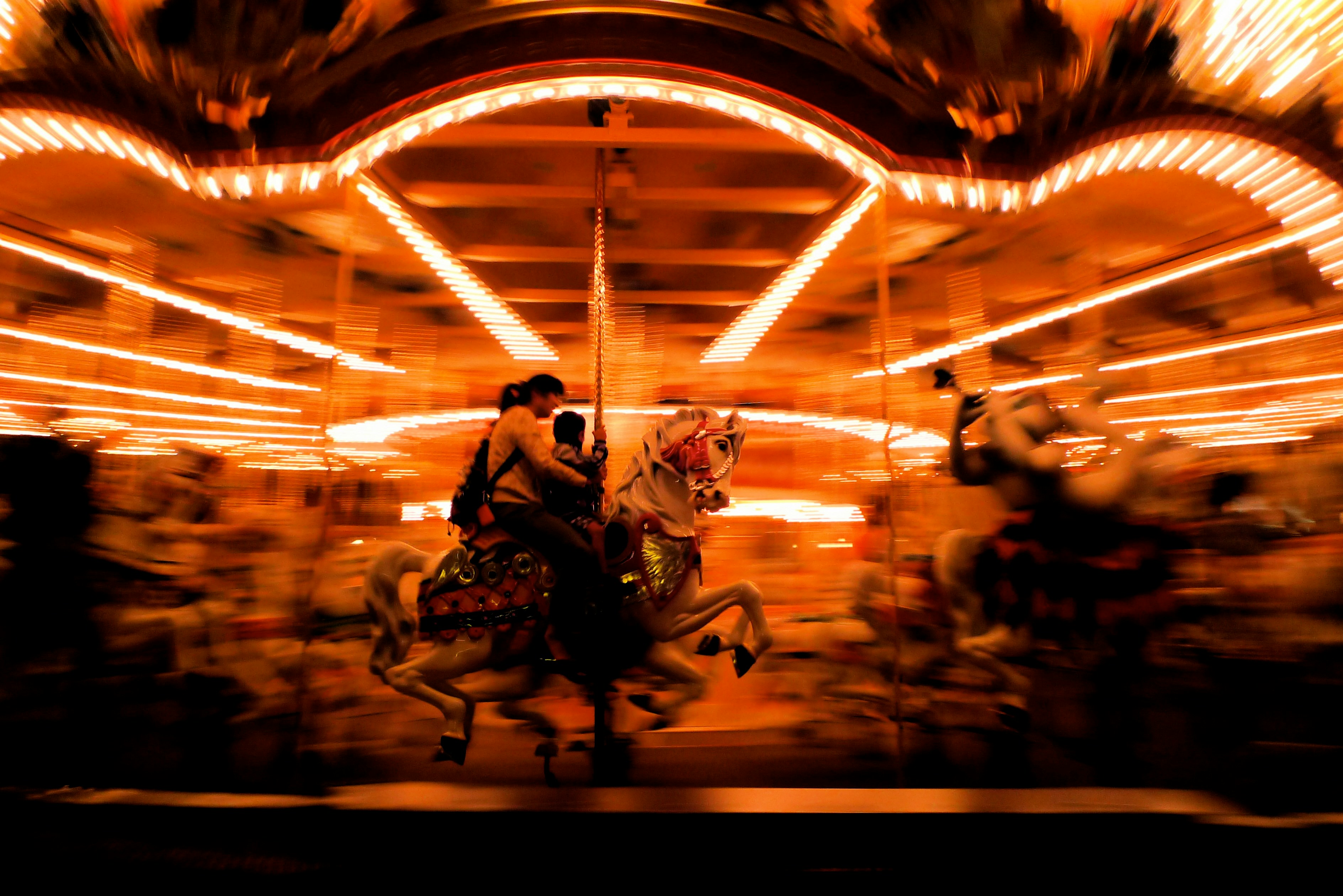Neon-lit carnival rides blurred in motion, evoking chaos and lost youth.