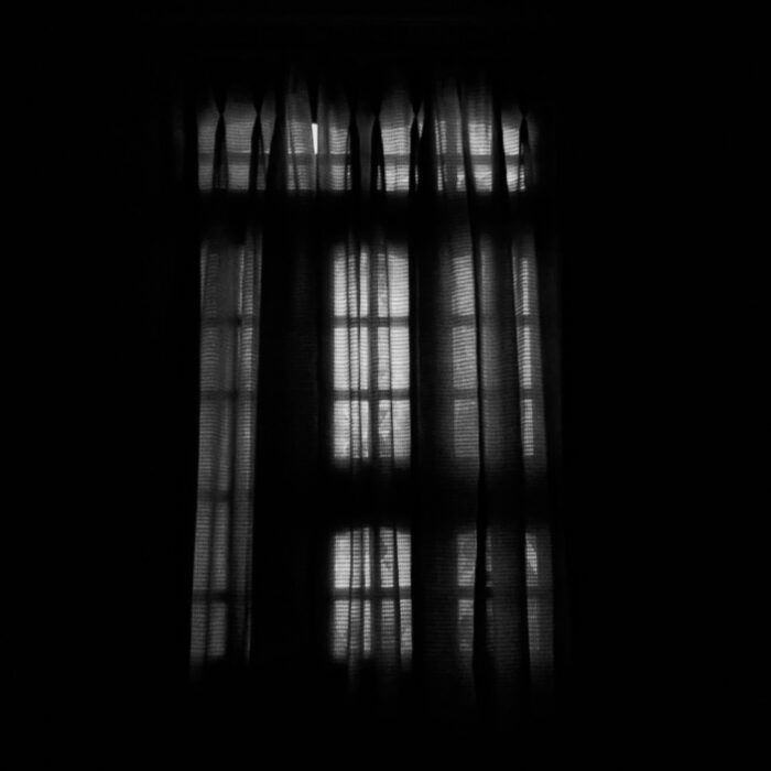 Barred window casting sharp shadows on a wall, evoking censorship and confinement