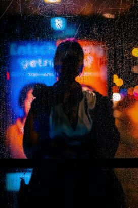 Blurred city lights seen through a scratched, rain-streaked window at night.