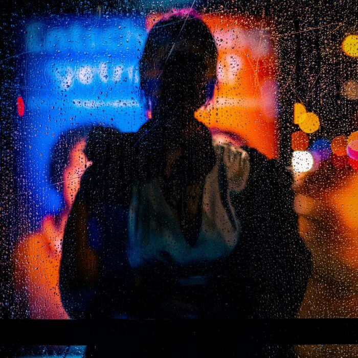 Blurred city lights seen through a scratched, rain-streaked window at night.