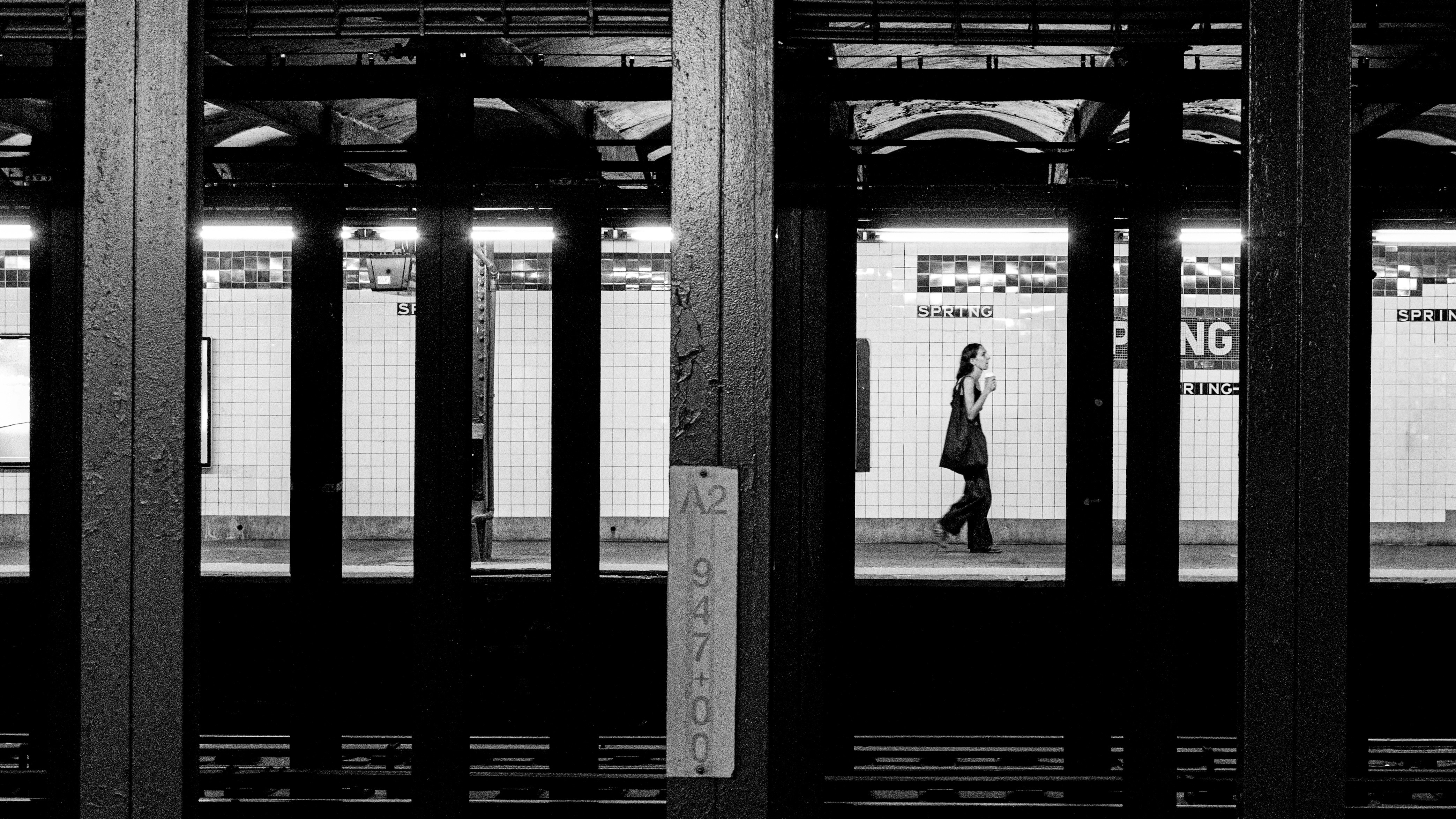 A woman walking alone through a subway station, seen through dark structural frames.