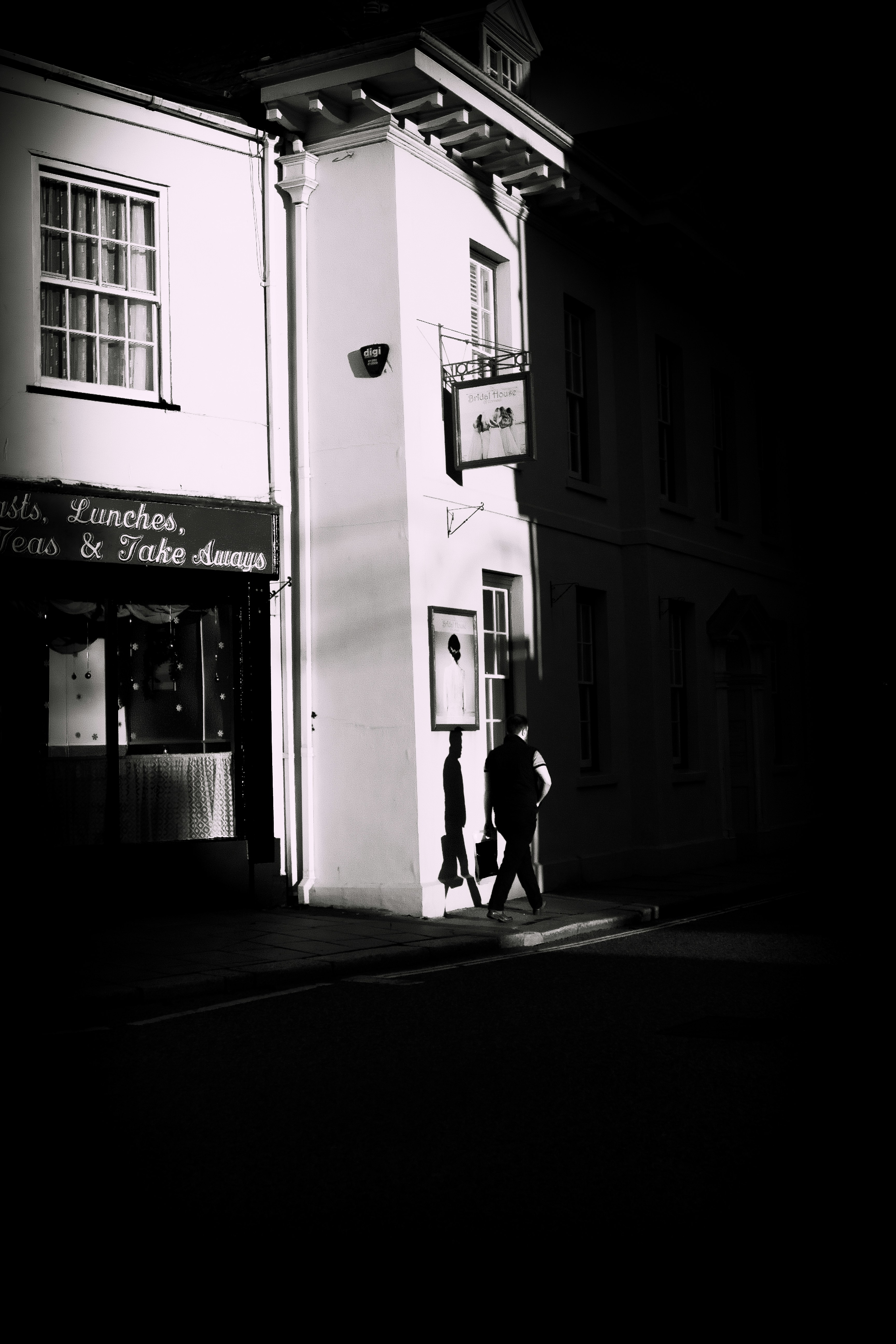 A lone man walking along a British street in strong evening light.