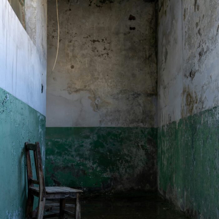 An empty, decaying room with a broken wooden chair against the wall.