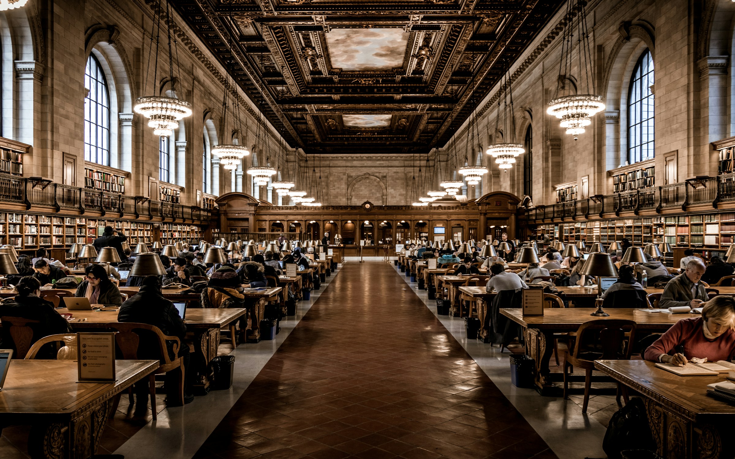 A reading room with long tables, lamps and bookshelves