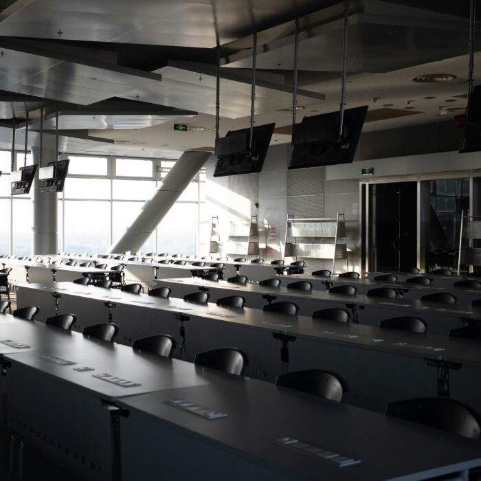 An empty corporate training room with rows of desks, chairs and suspended screens.