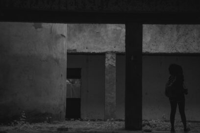 An abandoned industrial lot at night behind a chain-link fence, suggesting danger, neglect and a closed circle of violence.