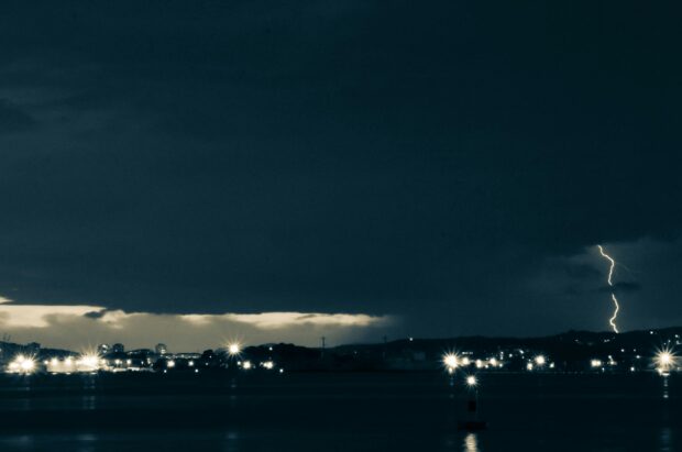 Lightning over harbour town at night with storm approaching – symbolic of unease and departure