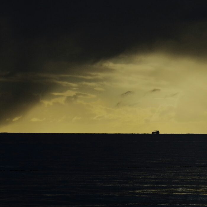 A small boat silhouetted against a stormy sea and horizon light.