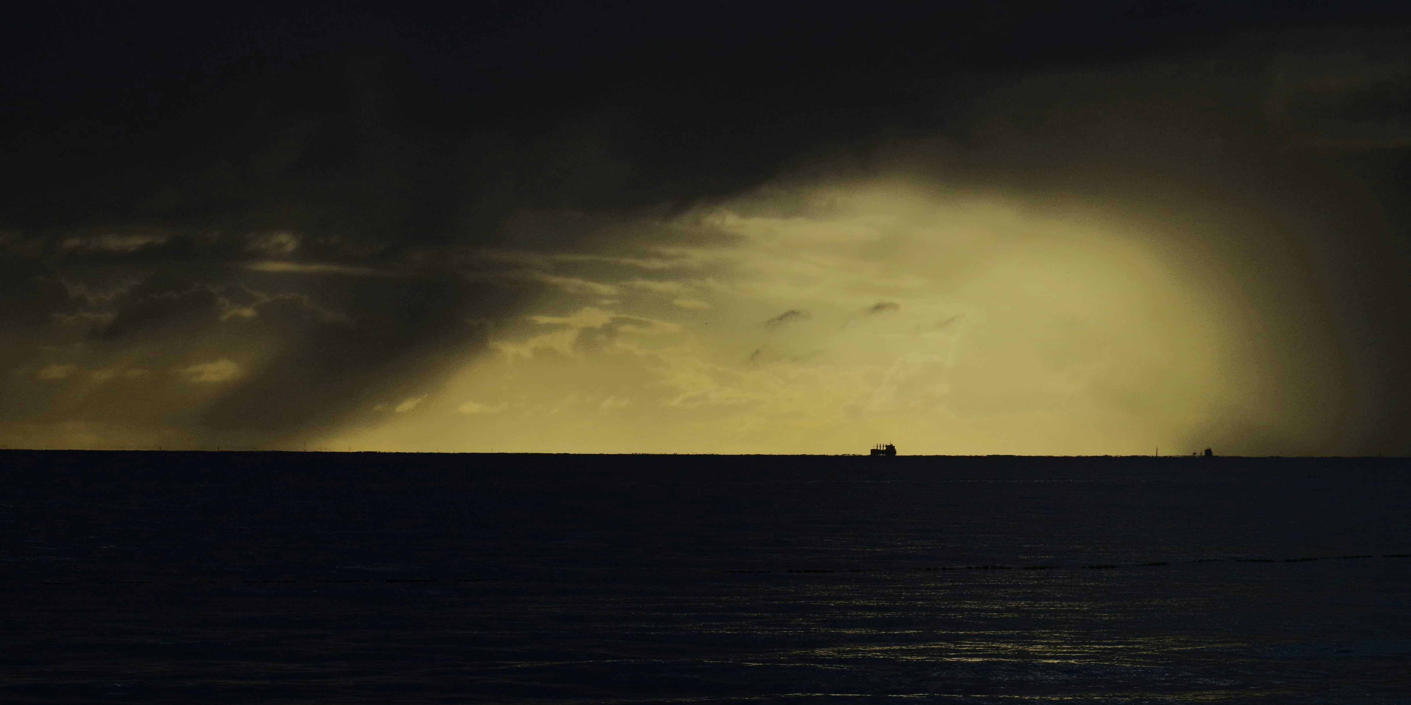A small boat silhouetted against a stormy sea and horizon light.