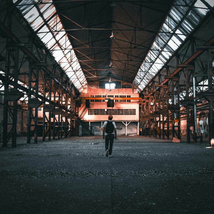 Stark, high-contrast industrial interior with sharp geometric lines and empty space, evoking themes of abandonment and toxic capitalism.