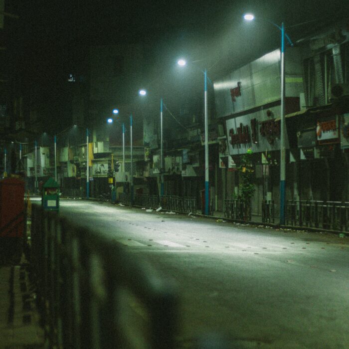 Dimly lit Lagos street at night, lined with lamps and shuttered shops, evoking memory, loss, and return.