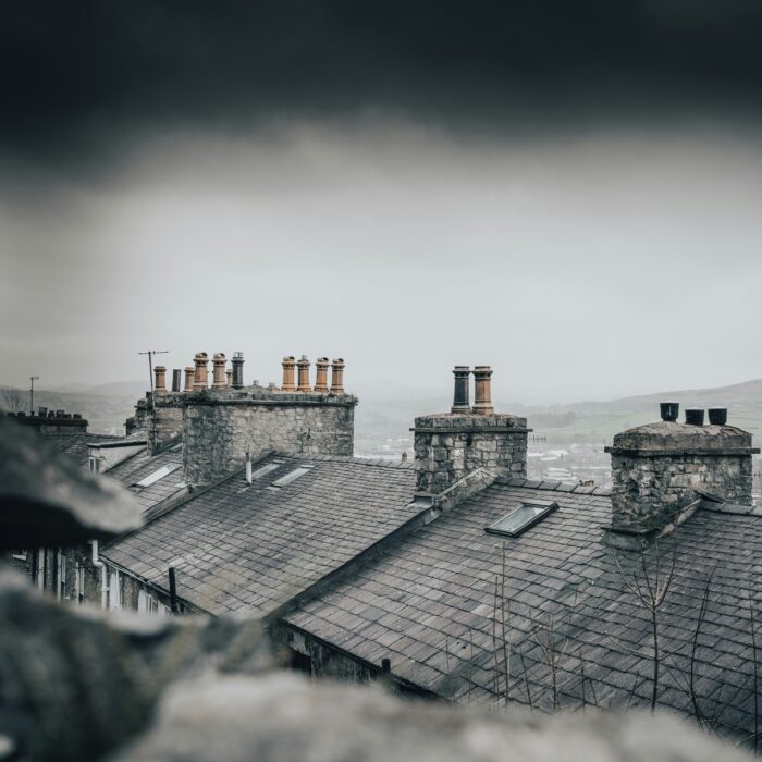 Dark rooftops with chimneys under a brooding Scottish sky, evoking grit and tension.