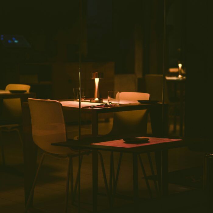 A dimly lit restaurant table set for two, one lamp glowing over empty chairs.