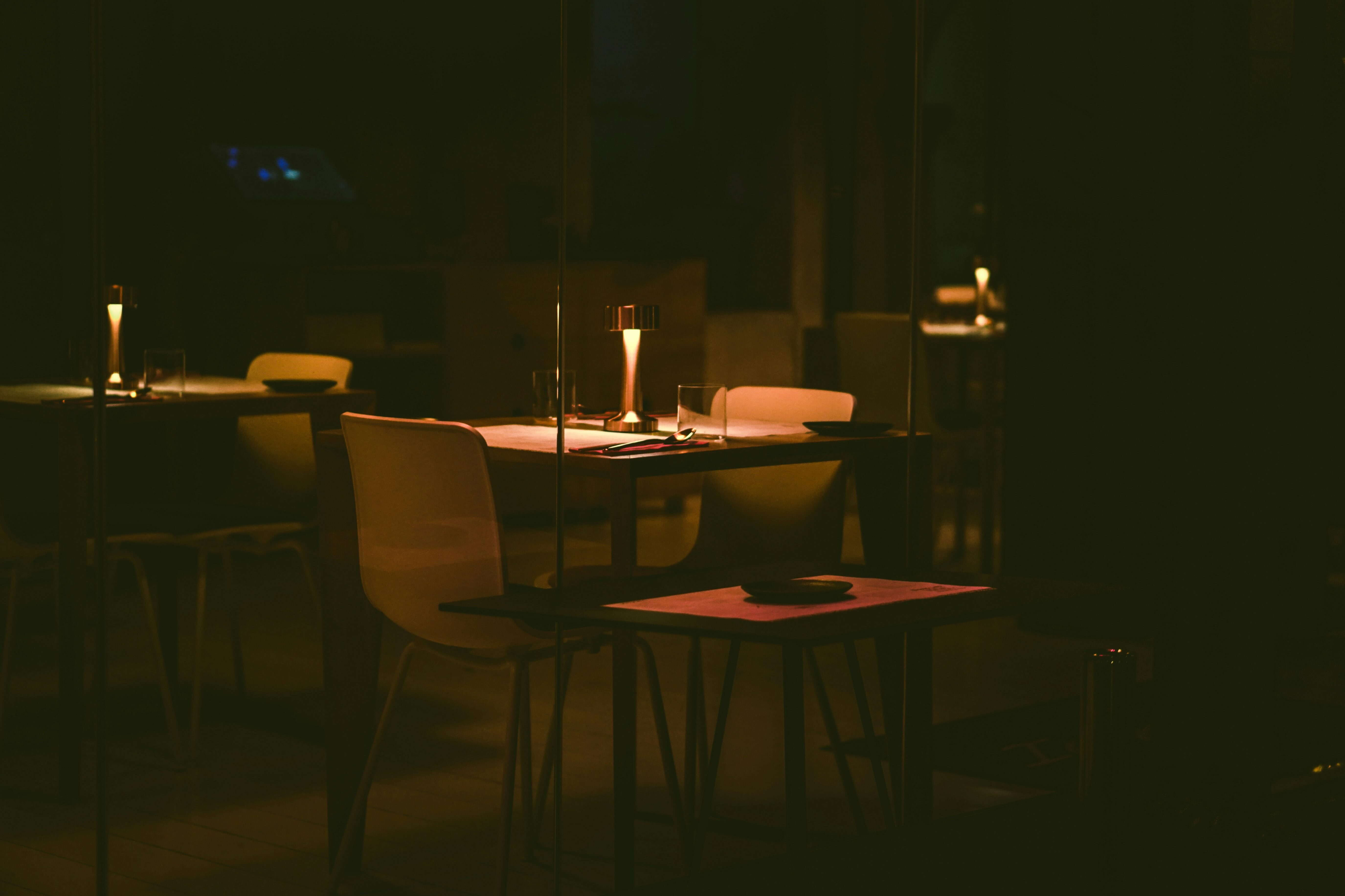 A dimly lit restaurant table set for two, one lamp glowing over empty chairs.
