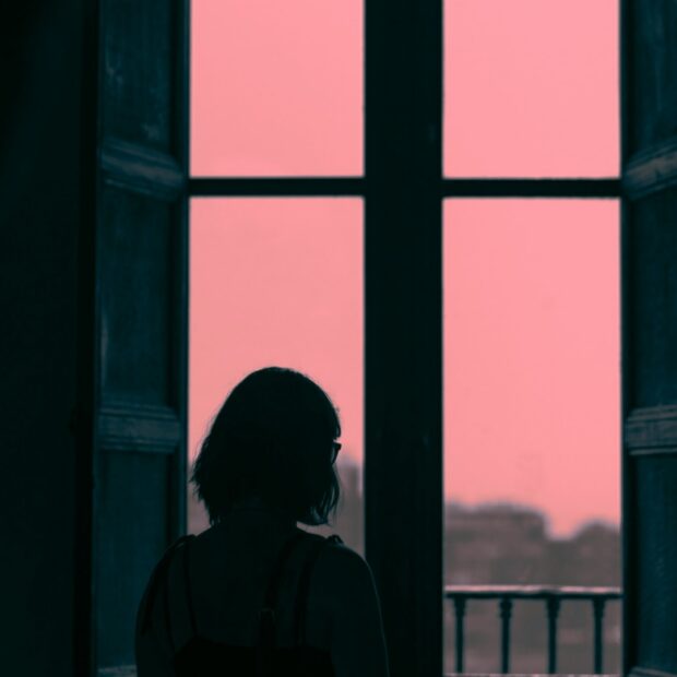 A woman sits alone at dusk in a quiet garden, the sky bright behind her.