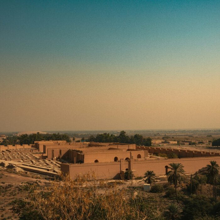 Earthen-walled historic city complex in a dry landscape with palm trees under a vast open sky