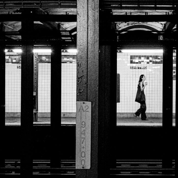 A woman walking alone through a subway station, seen through dark structural frames.