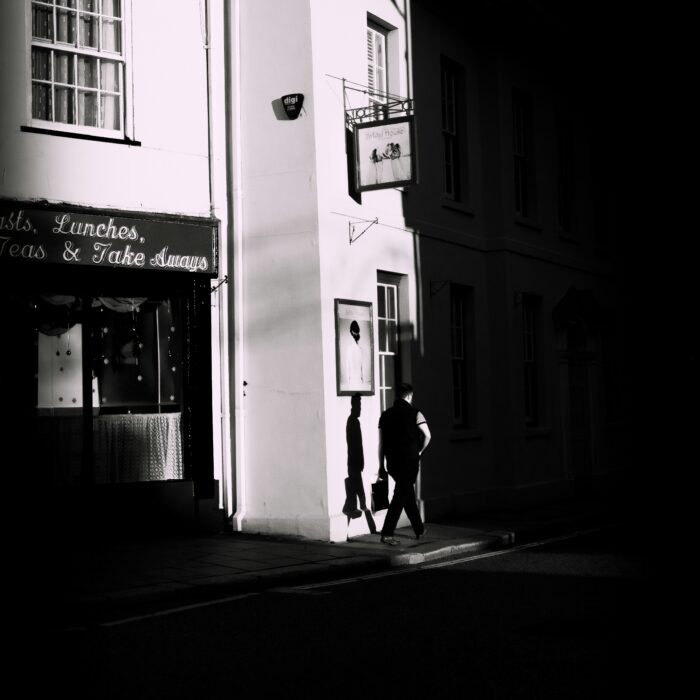 A lone man walking along a British street in strong evening light.