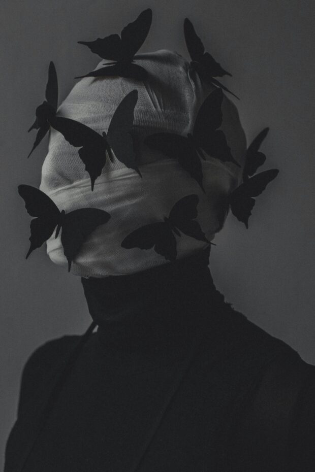 A blurred stage-lit figure surrounded by the suggestion of wings, evoking transformation, performance and unease.