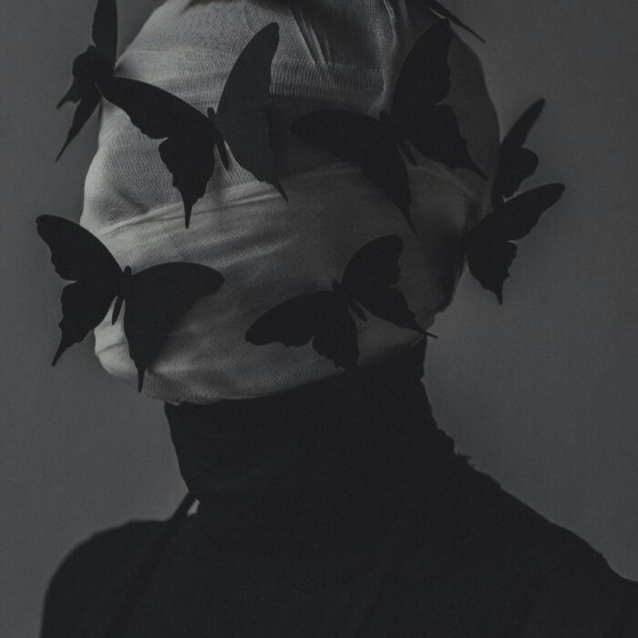 A blurred stage-lit figure surrounded by the suggestion of wings, evoking transformation, performance and unease.
