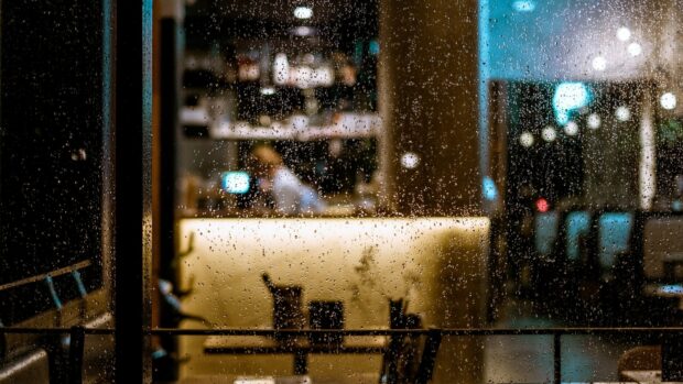 An elderly woman sitting alone at a café table beside a bright window.