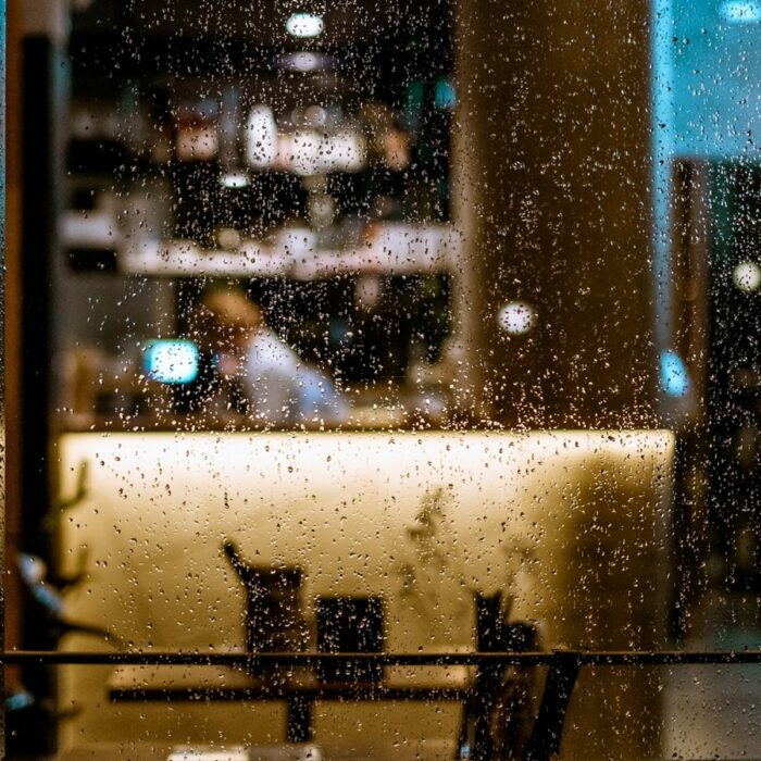 An elderly woman sitting alone at a café table beside a bright window.