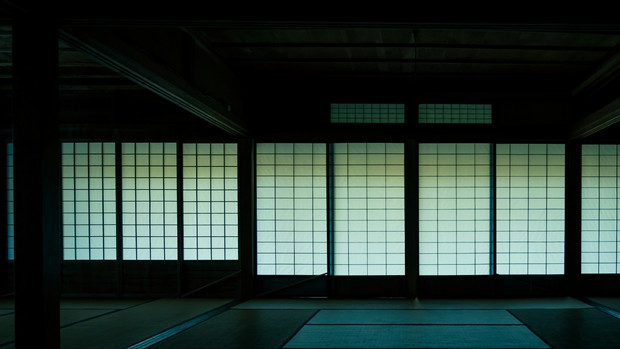 An empty, dimly lit room with tatami flooring and luminous panelled screens.