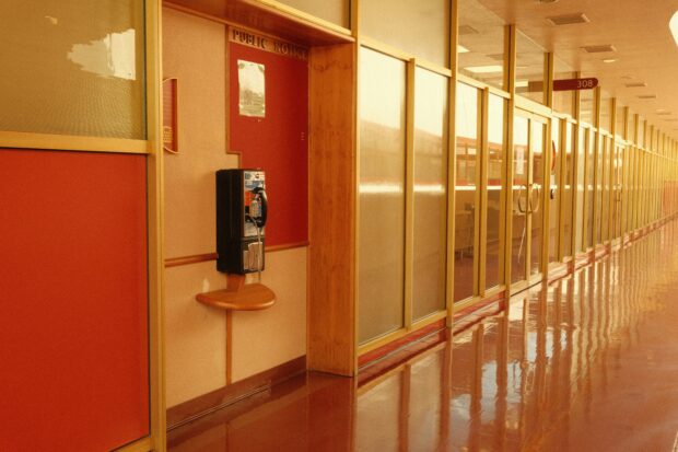 Empty institutional corridor with red panels, a public notice board and a wall-mounted payphone.