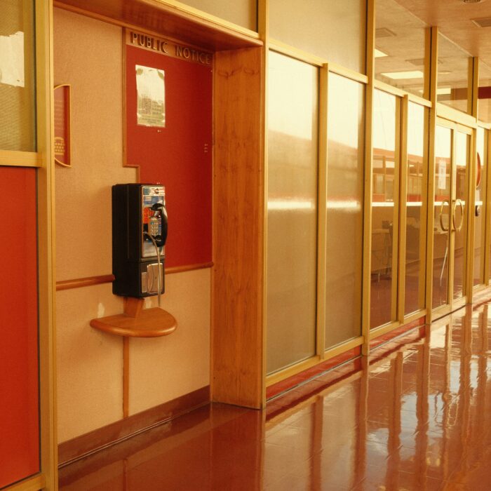 Empty institutional corridor with red panels, a public notice board and a wall-mounted payphone.