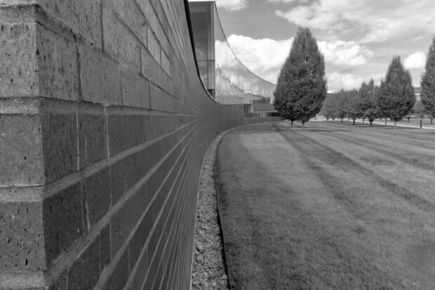 A black-and-white institutional building beside clipped grass and trees, evoking a controlled public space.