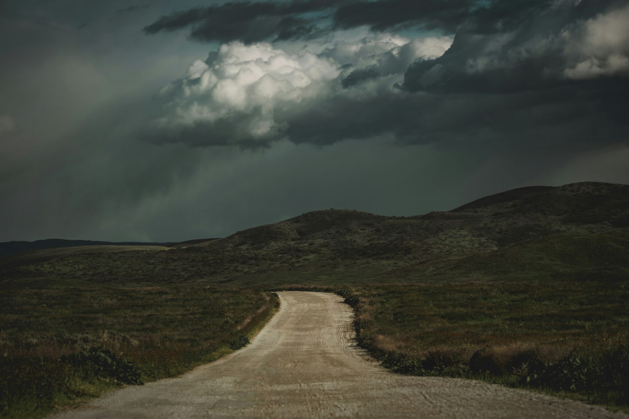 A dirt road running into hills under a storm sky