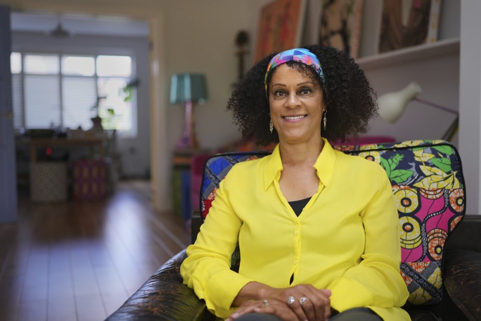 Bernardine Evaristo seated at home in a yellow blouse and patterned headwrap
