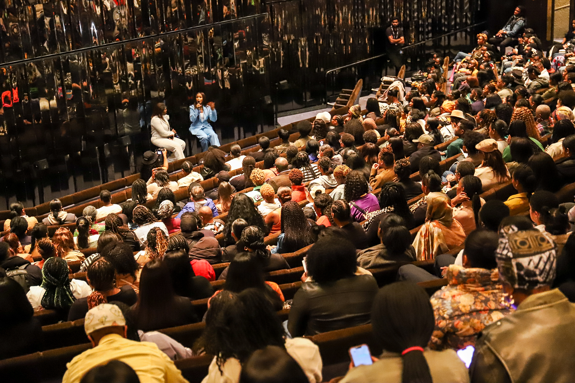 A packed auditorium at the Black British Book Festival, the audience facing two speakers in conversation on a lit stage