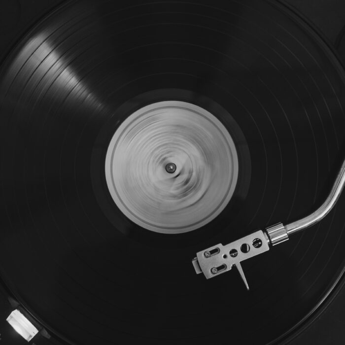 A black vinyl record turning on a turntable, photographed from above in monochrome.